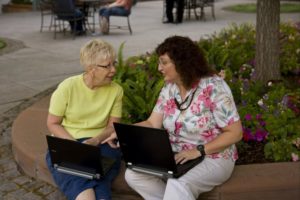 Two women indexing on laptops at a park